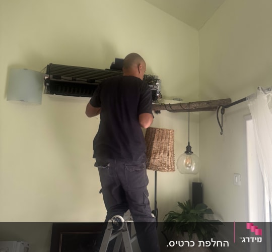אדם על סולם מתקן מזגן על קיר